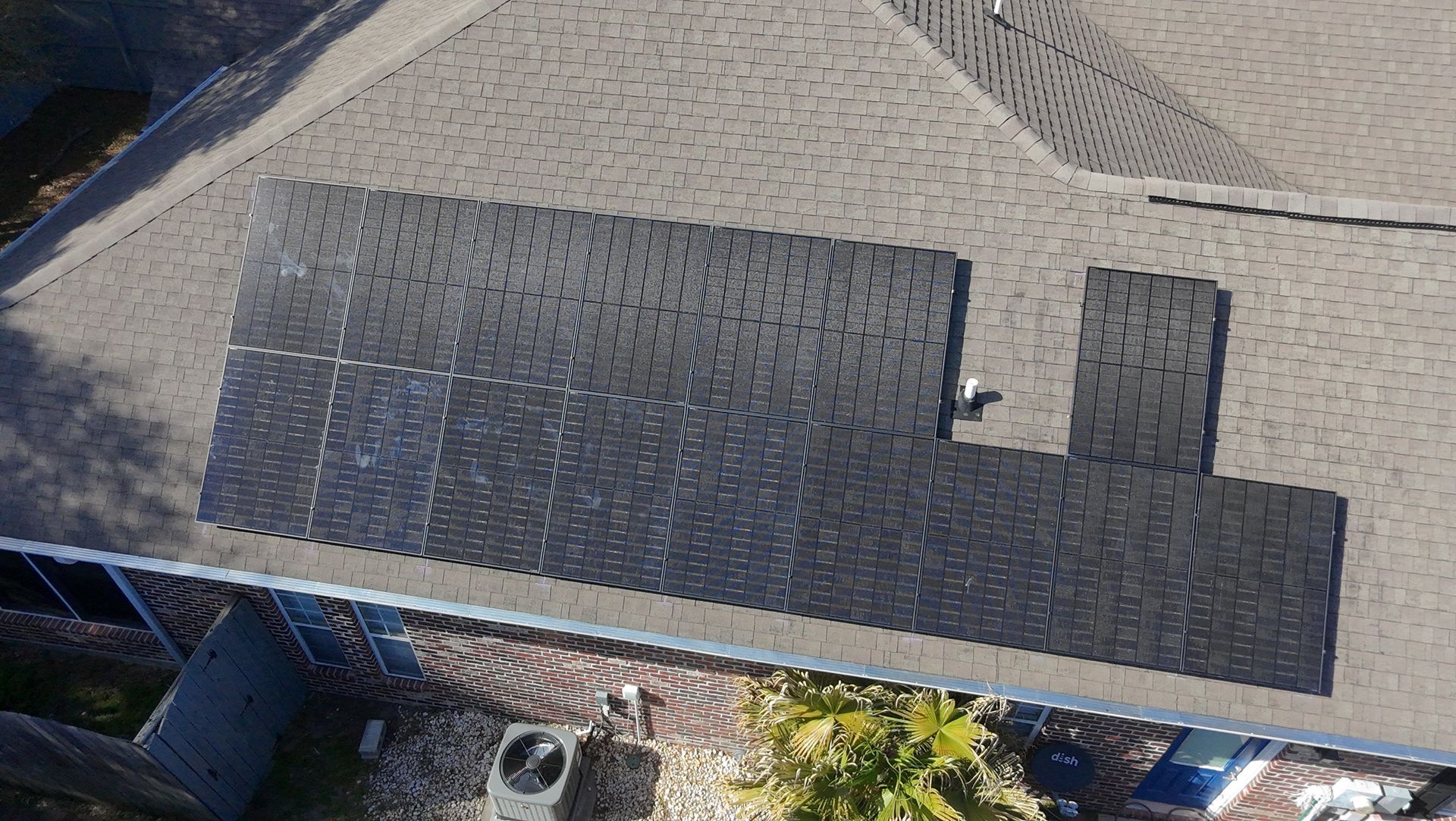 Solar panels installed on a brown-shingled roof of a house.