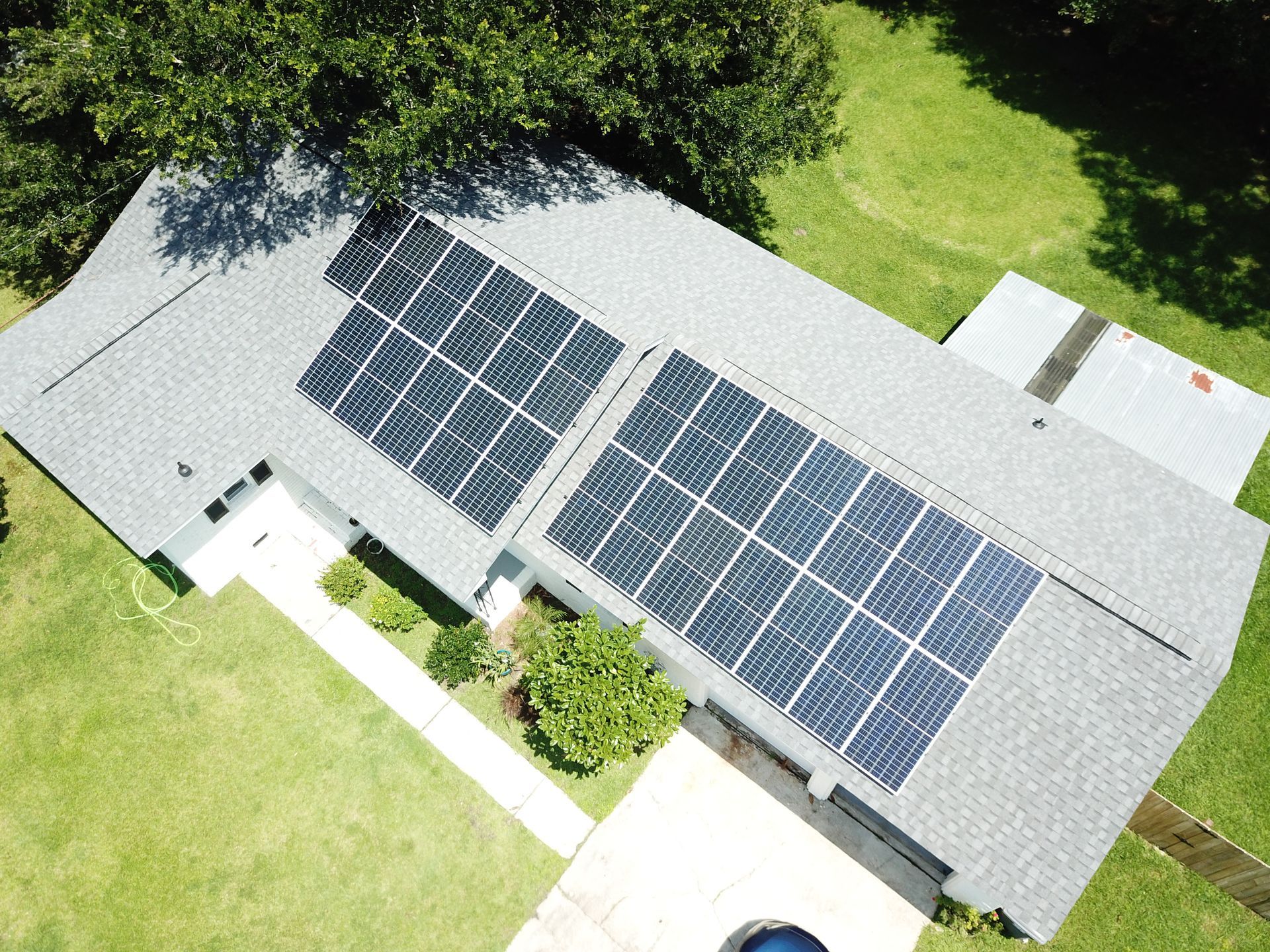 Aerial view of a house with solar panels on the gray roof and green grass surrounding.