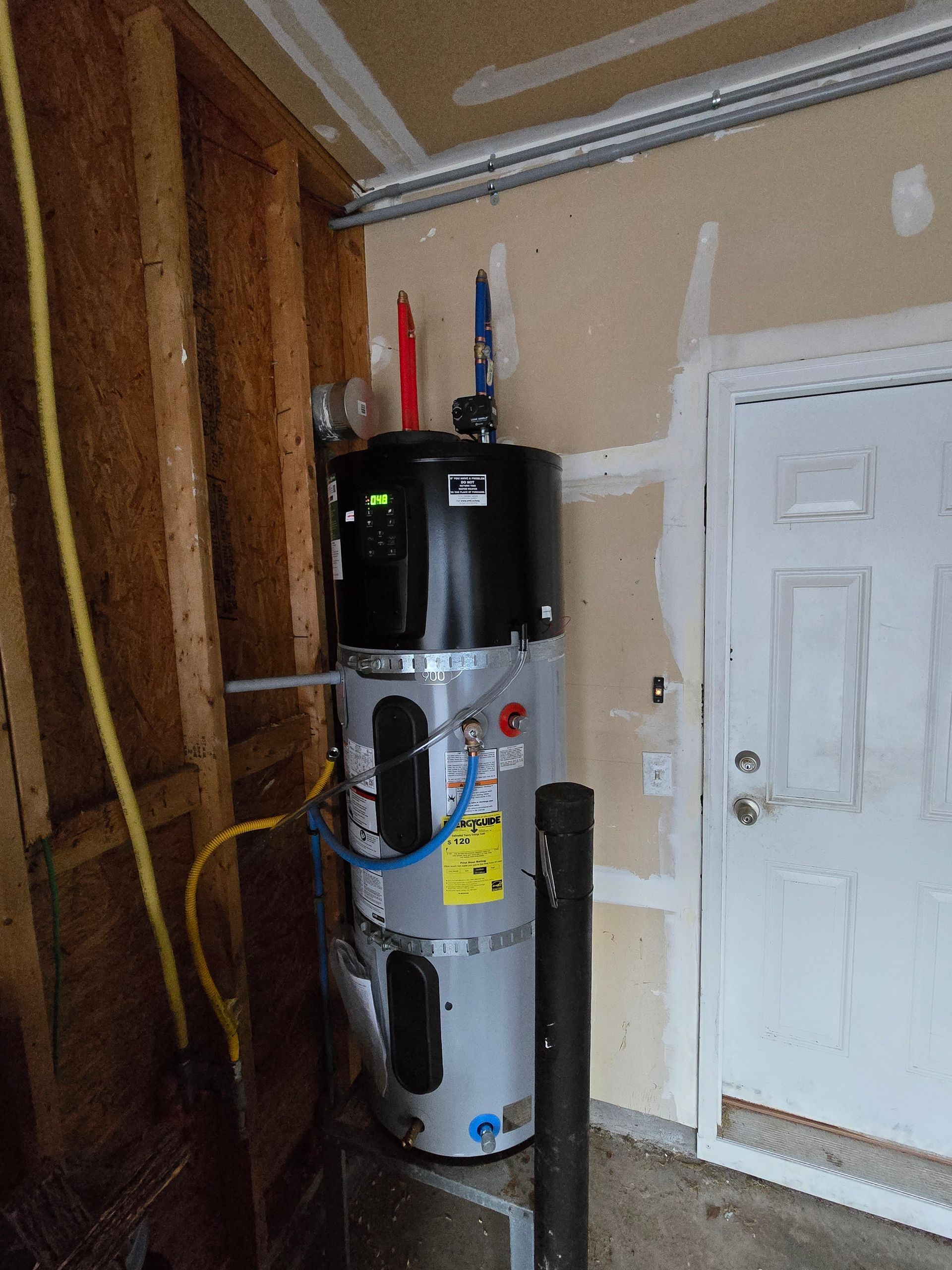 A two-part electric water heater installed in a garage, with attached pipes and venting.