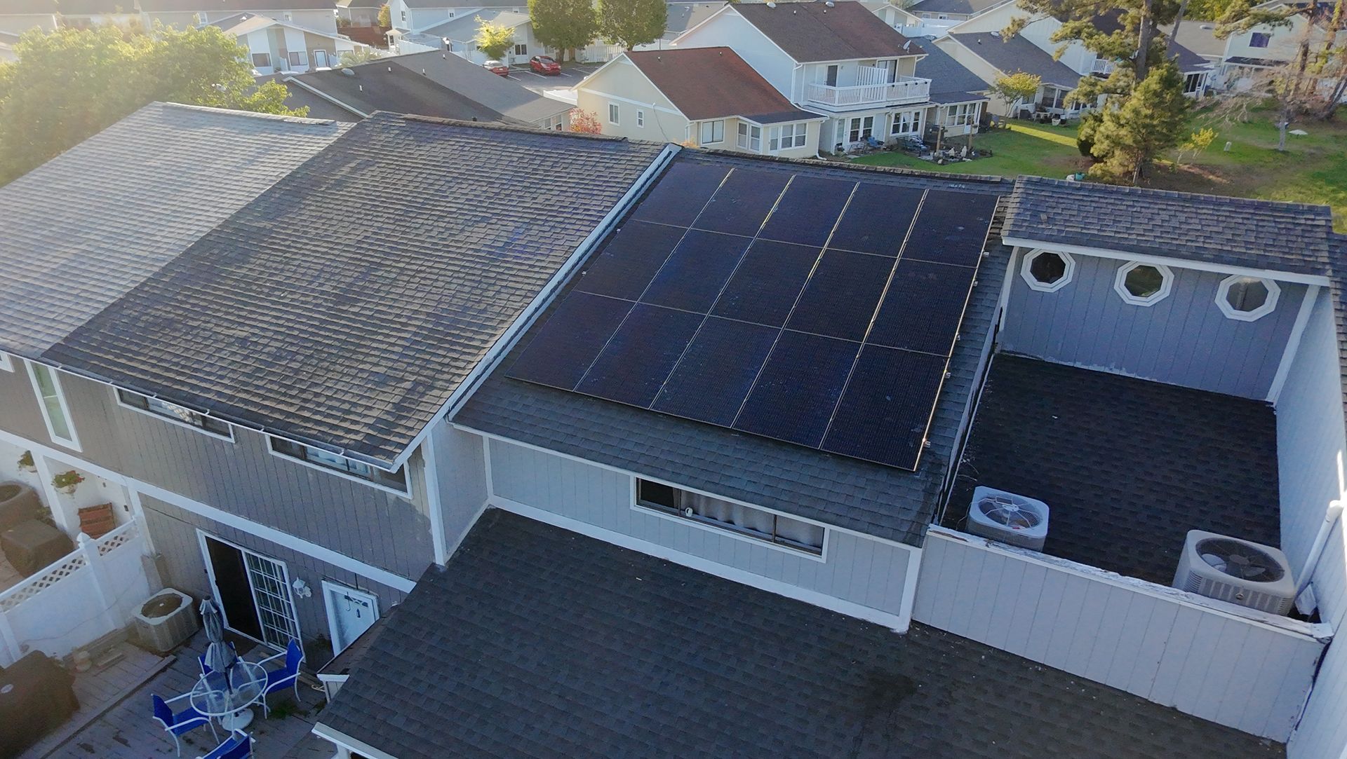 Rooftop with solar panels installed on a residential home. Other houses and the street are visible in the background.