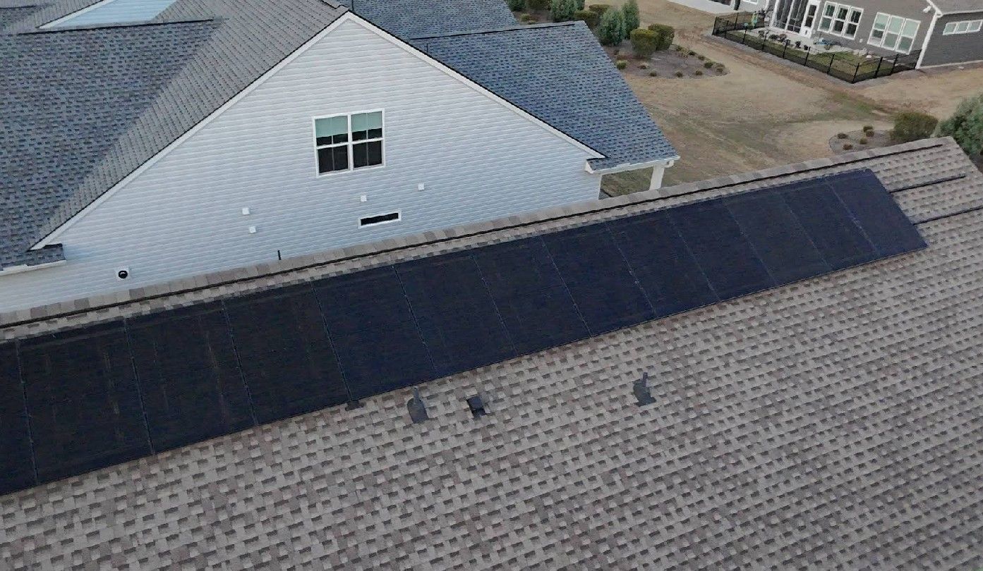 Overhead view of a house roof with a long line of black solar panels installed on the surface.