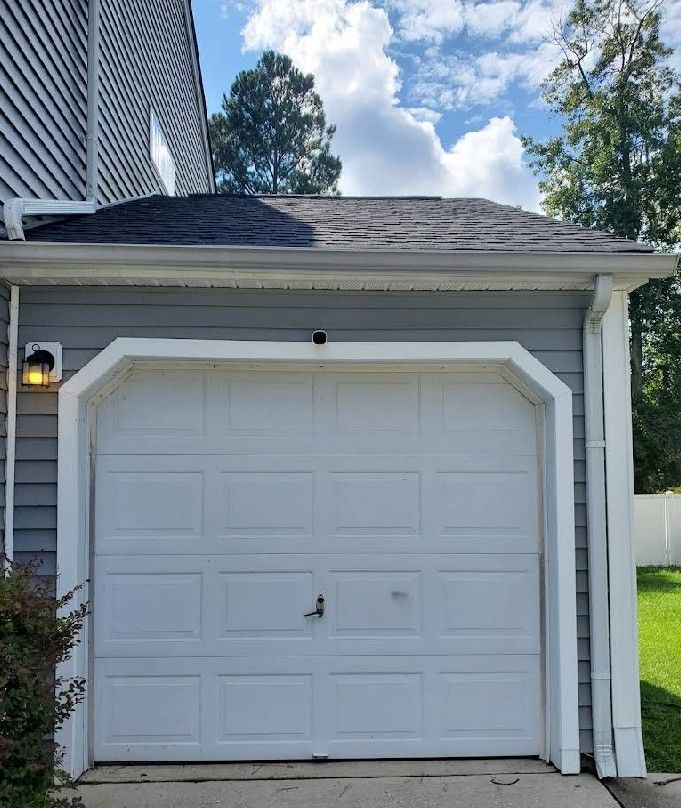 White garage door on a gray building with a dark roof and white trim under a blue sky.
