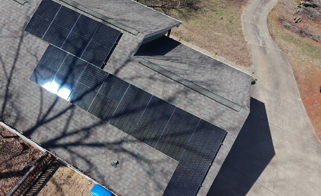 Solar panels on a gray roof, reflecting sunlight. A driveway is visible on the right.