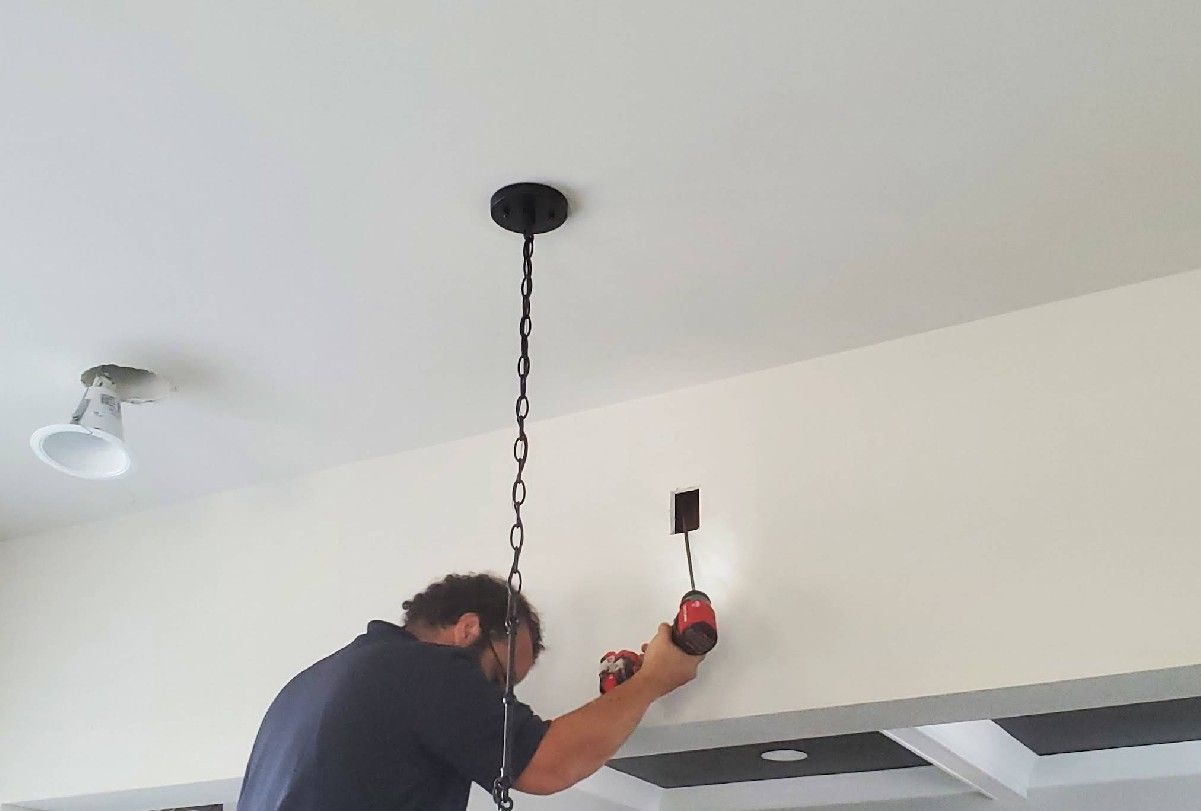 Man installing electrical wiring in a wall. A ceiling light fixture hangs above.