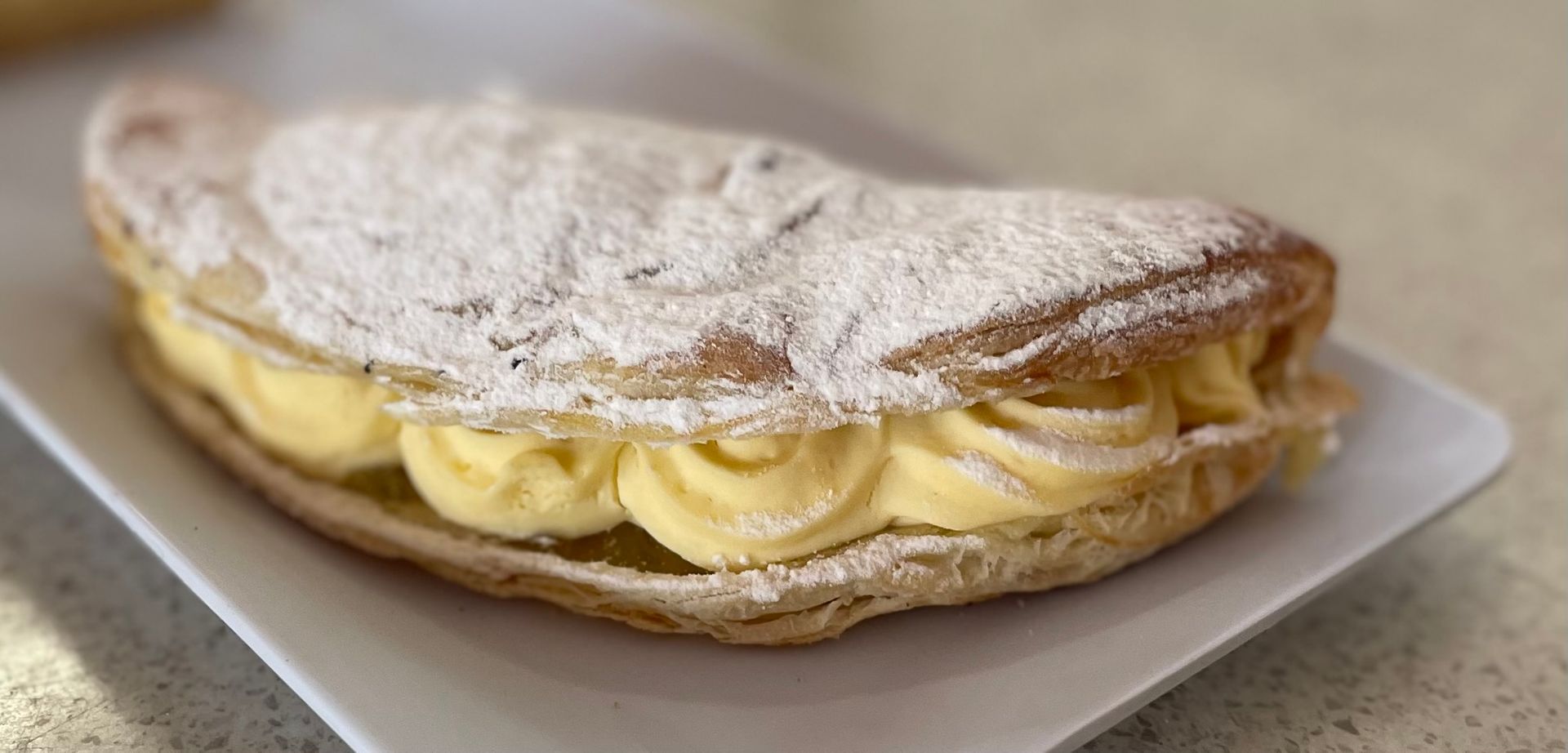 Pastry with cream filling, dusted with powdered sugar, on a white plate— Bread Basket in Kurri Kurri, NSW