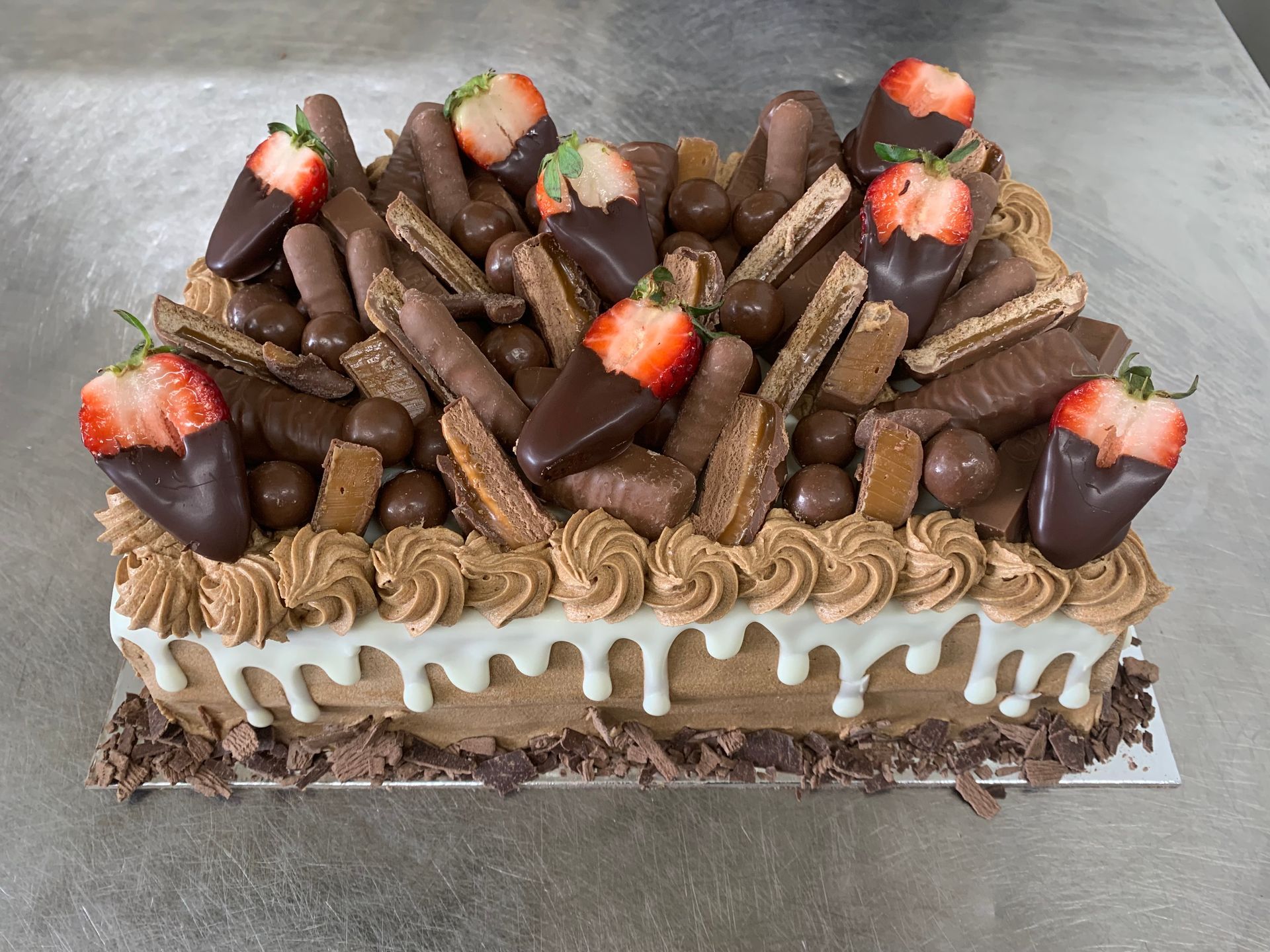 Chocolate cake with frosting, candy bars, chocolate-covered strawberries, and white icing drips— Bread Basket in Kurri Kurri, NSW