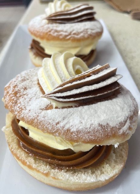 Two cream-filled donuts with chocolate and vanilla swirls on a white plate, dusted with powdered sugar— Bread Basket in Kurri Kurri, NSW
