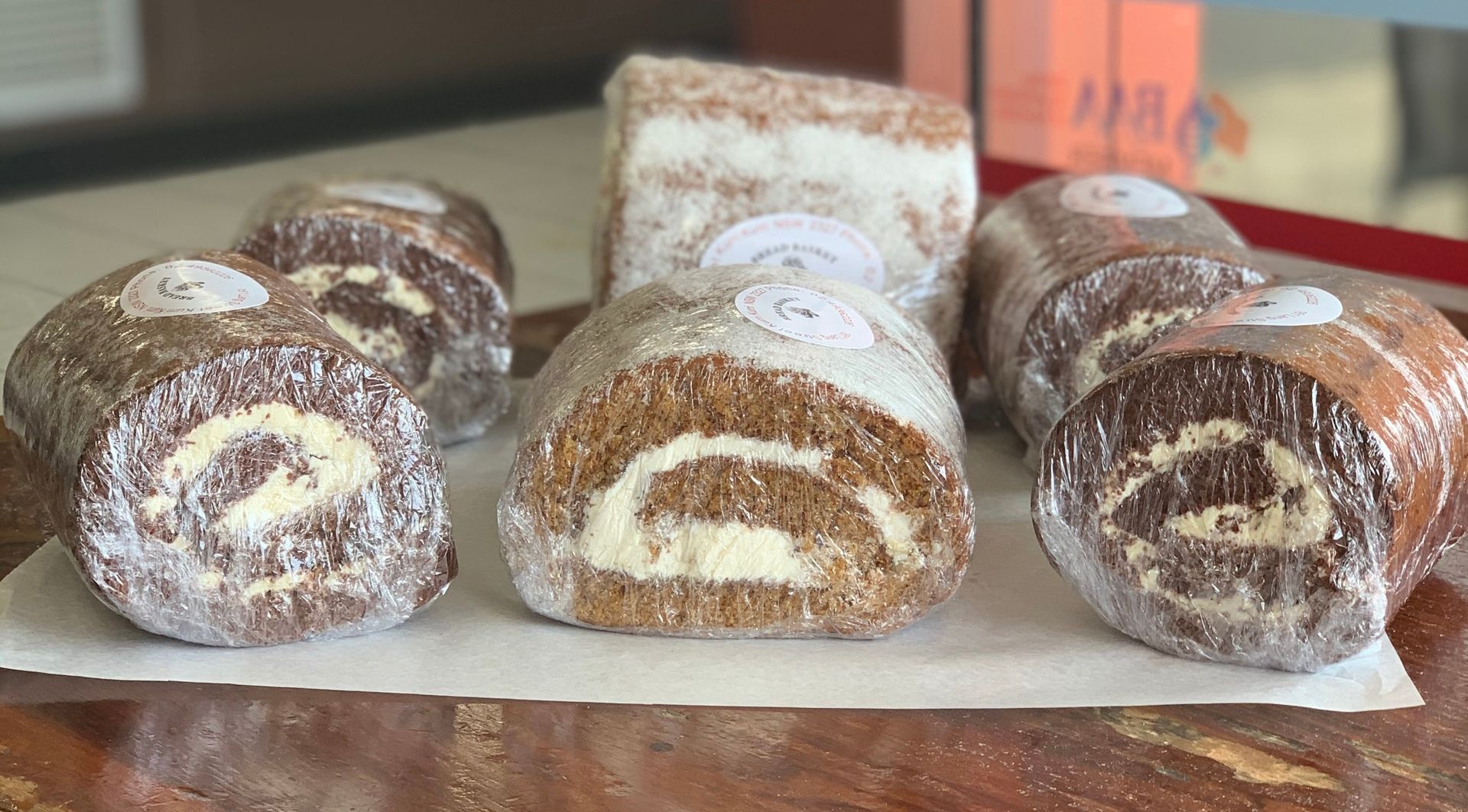 A pile of cakes wrapped in glad wrap on a table — Bread Basket in Kurri Kurri, NSW