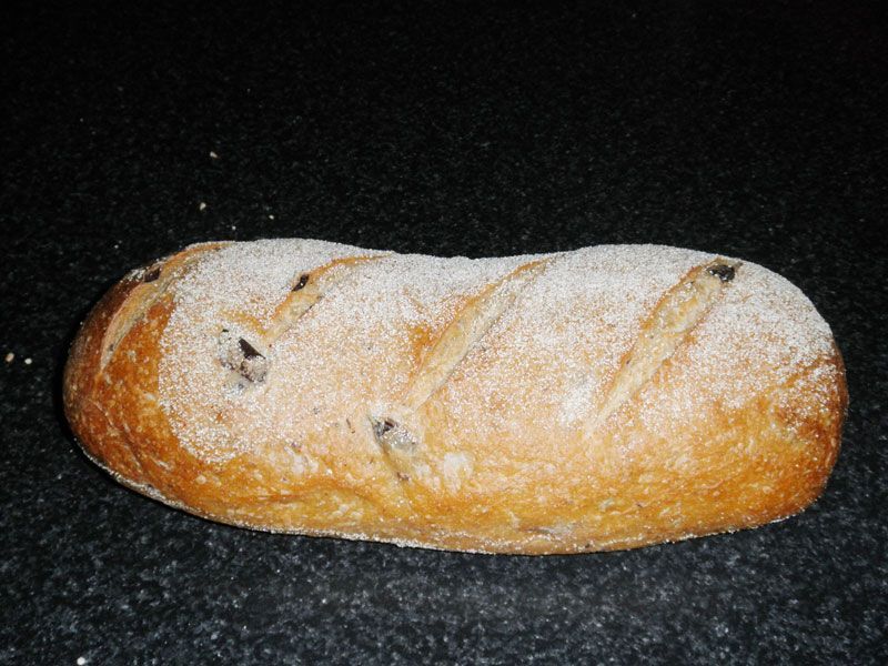 Loaf of olive bread on a dark, speckled surface. Bread is dusted with flour, has diagonal scores. — Bread Basket in Kurri Kurri, NSW