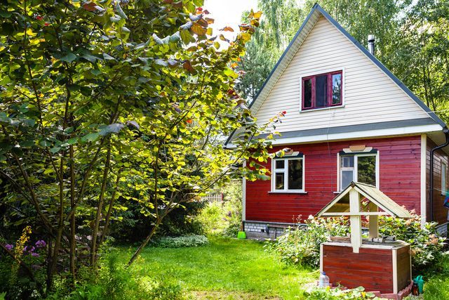 Red and white house with a well in a green, sunny yard, surrounded by trees.