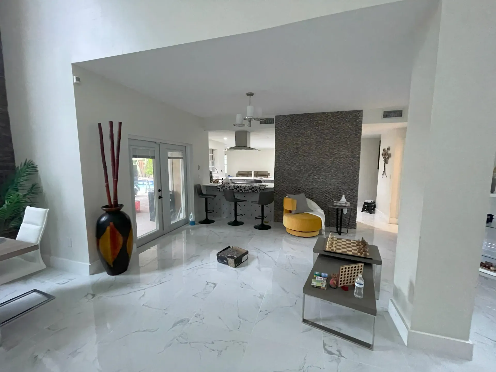 Modern open-plan living room with white tile floors, gray decor, and a kitchen in the background
