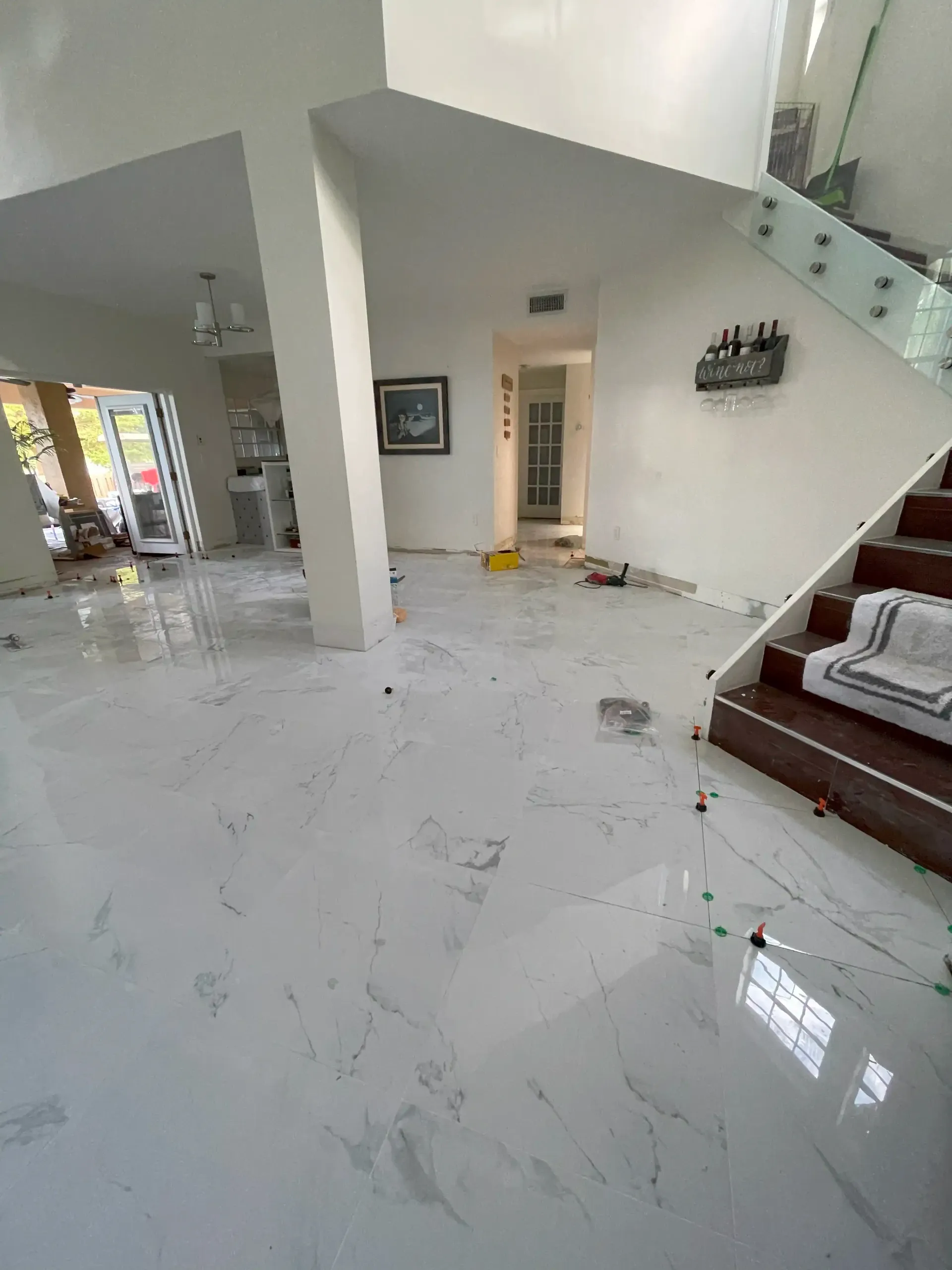 Bright living room with white marble floor, staircase wall, and wooden sofa along the right side.