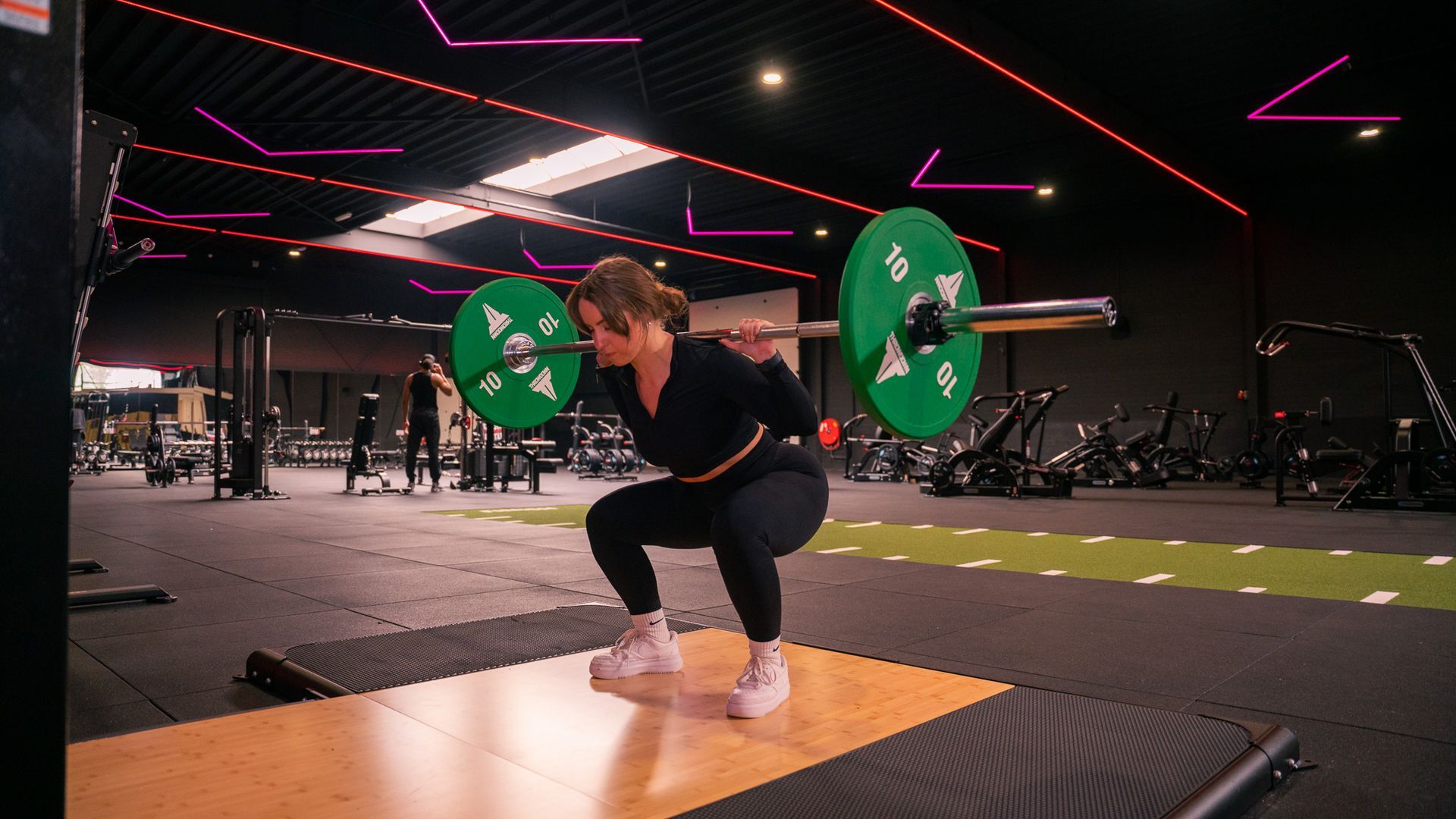 Een vrouw is aan het squatten met een halter in een sportschool.