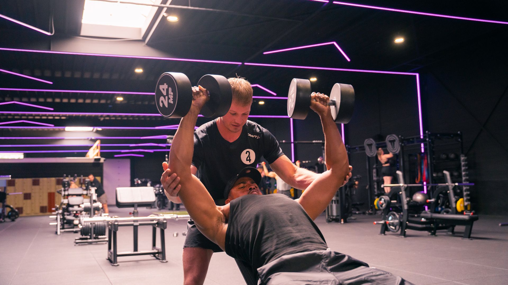 Een man helpt een andere man met het tillen van dumbbells in een sportschool.