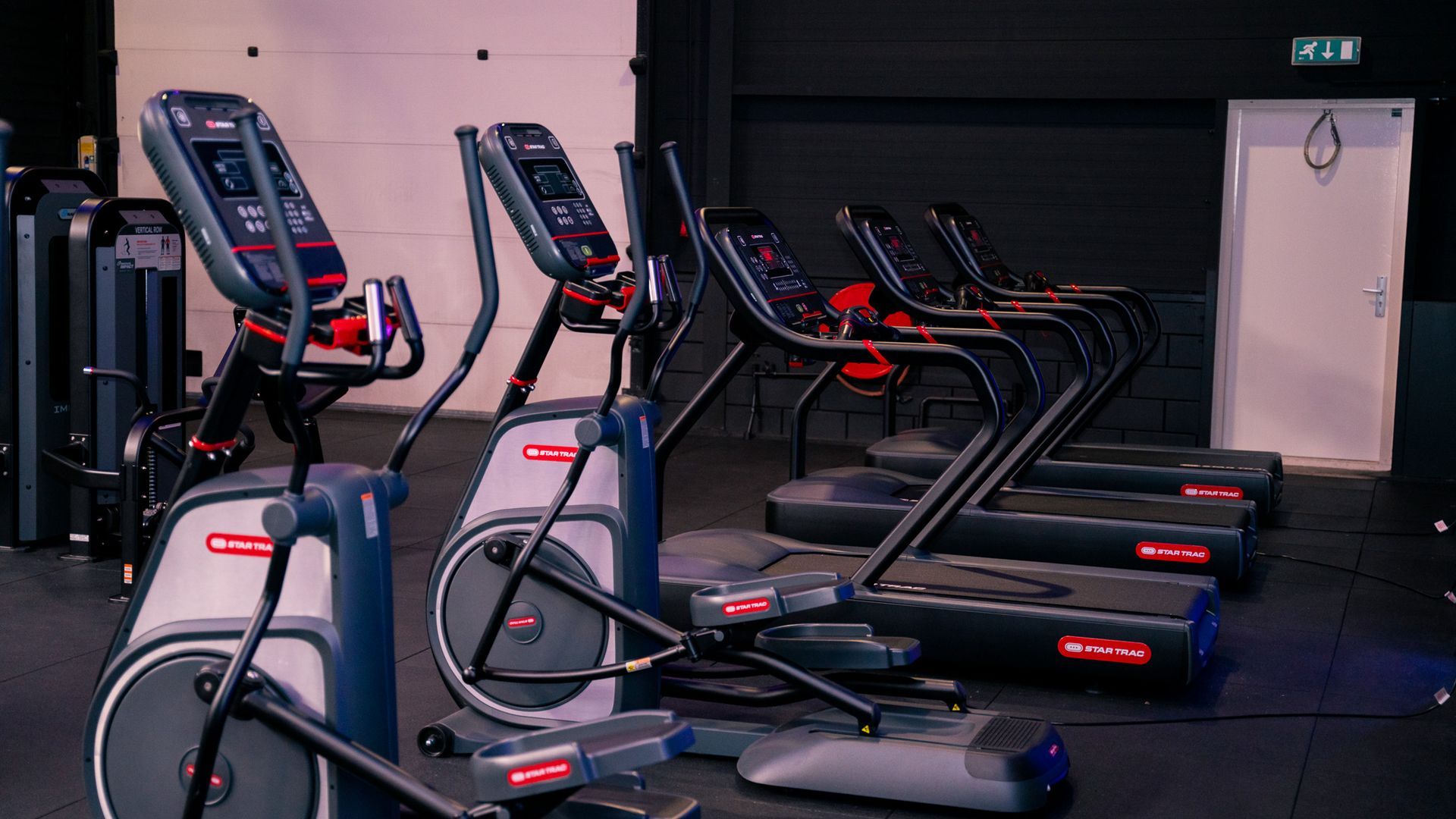 Een rij loopbanden en crosstrainers in een sportschool.