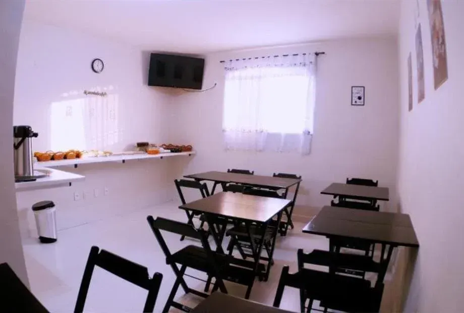 Sala branca com mesas e cadeiras dobráveis ​​pretas, um balcão com comida e uma TV.