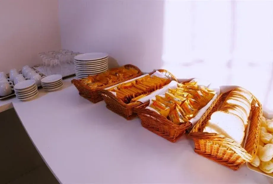 Pães e bolachas em cestas sobre uma bancada branca, ao lado de uma pilha de pratos e xícaras.