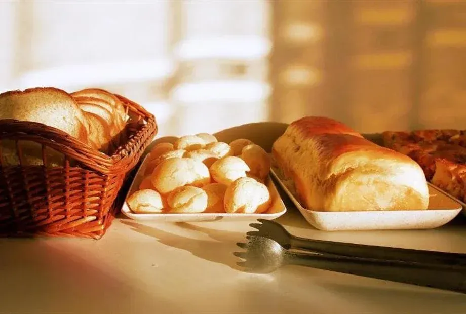 Variedade de pães: pães, pãezinhos e fatias em cestas e bandejas, com pinças para servir.