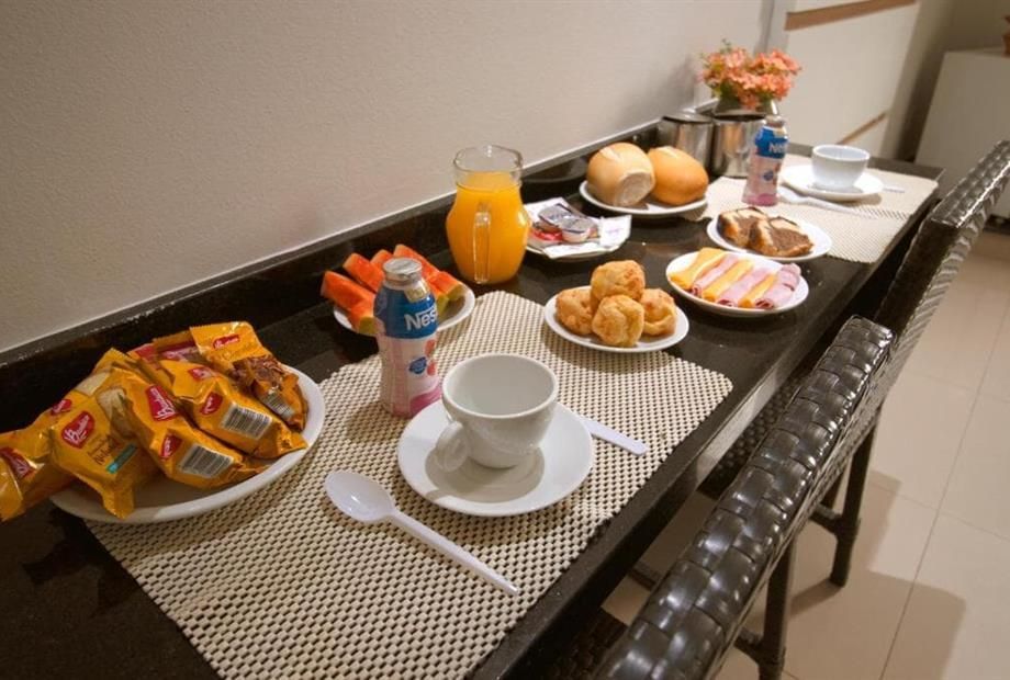 Mesa posta com opções de café da manhã: doces, suco, frutas e café.