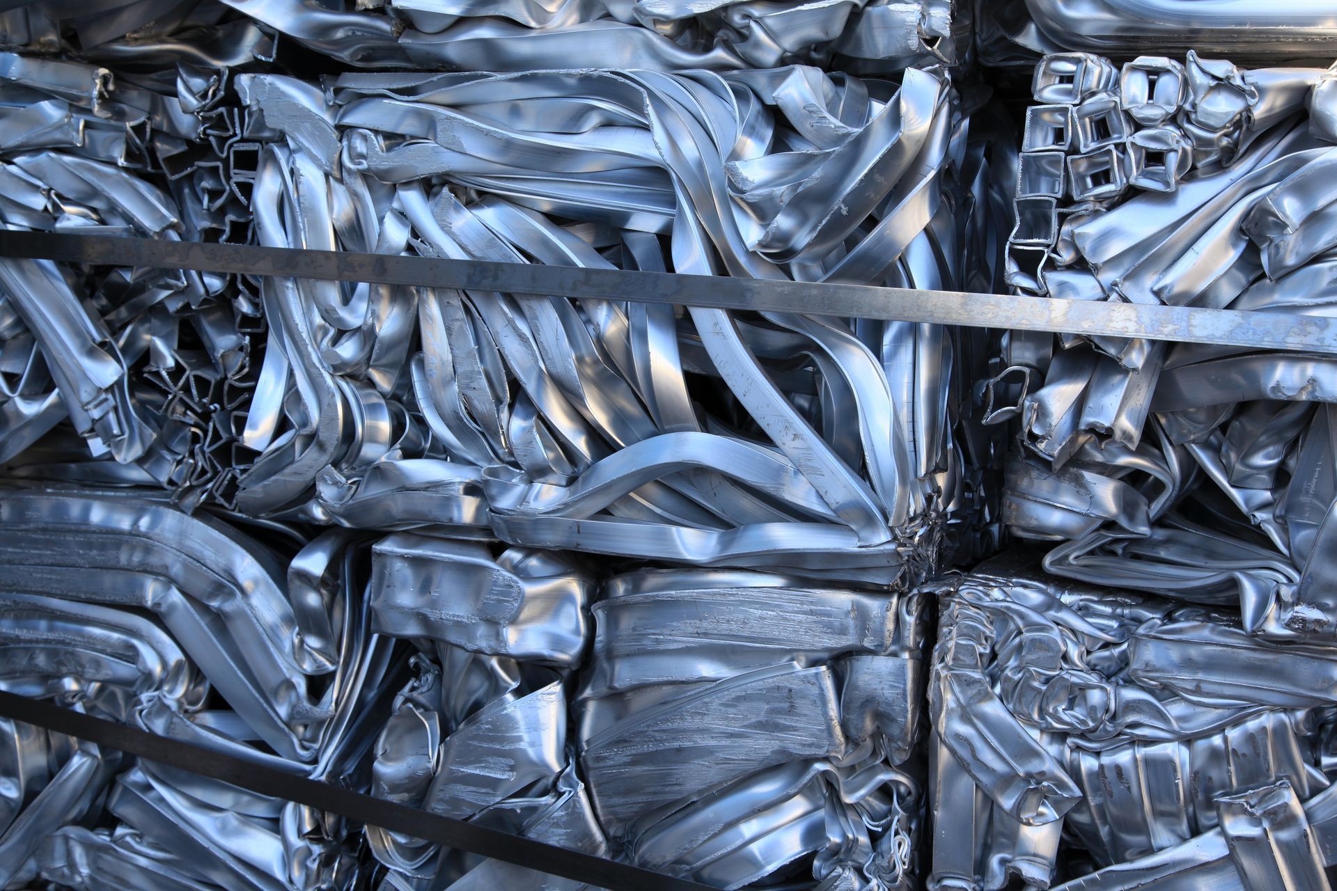 Compressed bundles of shiny aluminum scrap metal tightly packed and strapped, ready for recycling. Compressed bundles of shiny aluminum scrap metal tightly packed and strapped, ready for recycling.