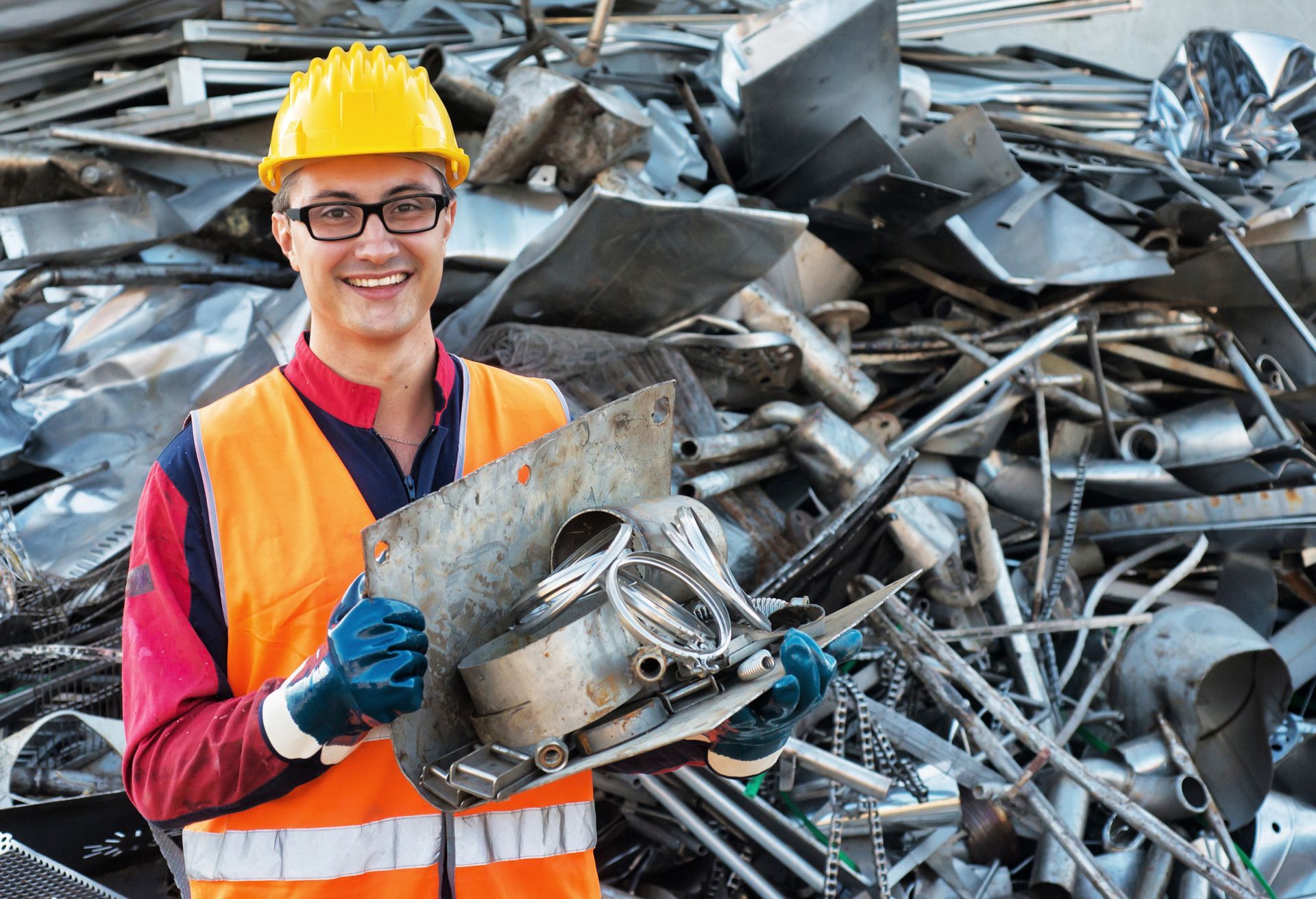 Smiling worker in safety gear at a metal landfill, offering scrap metal dealer services.