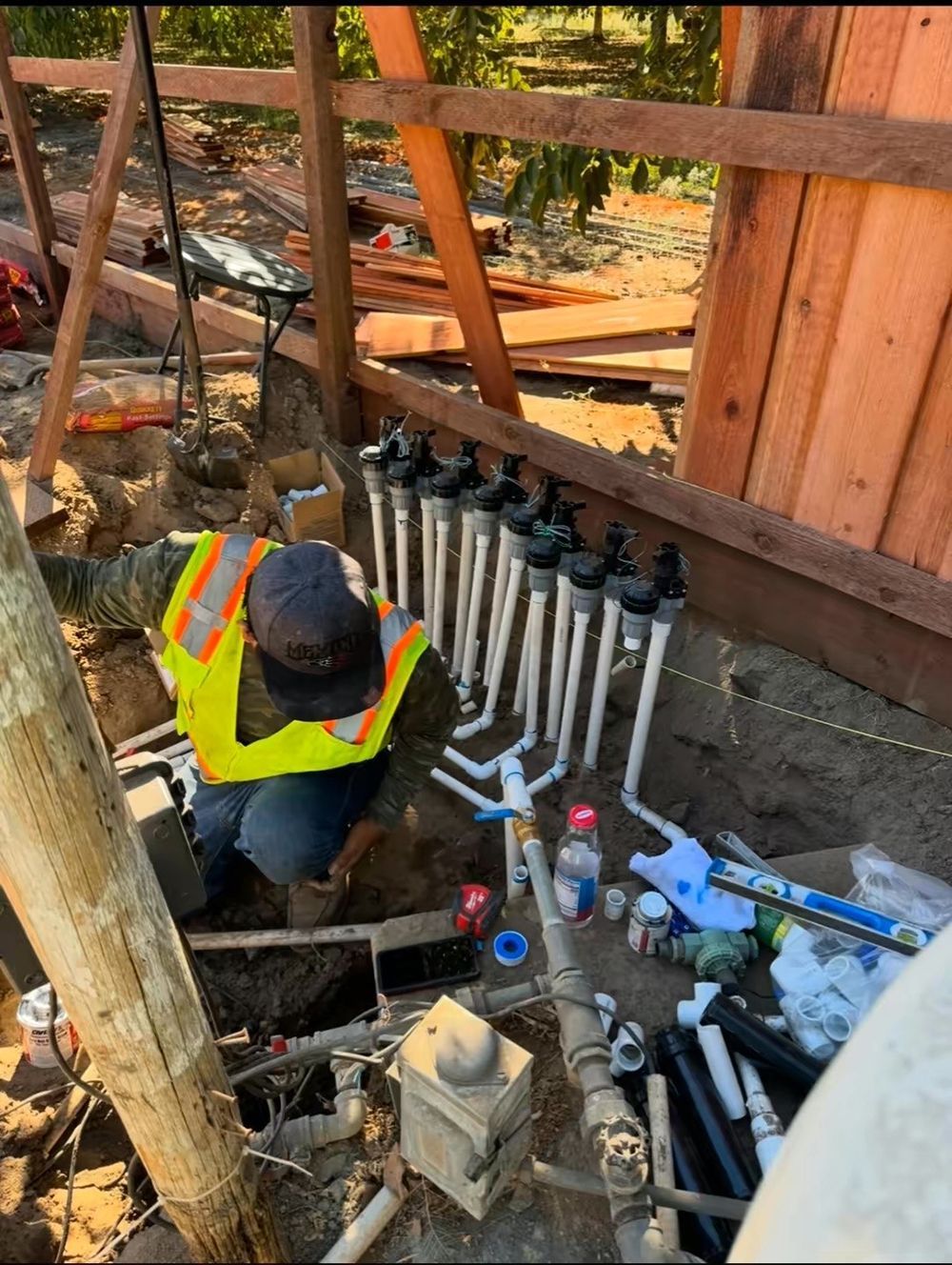 A man in a yellow vest is working on a sprinkler system.