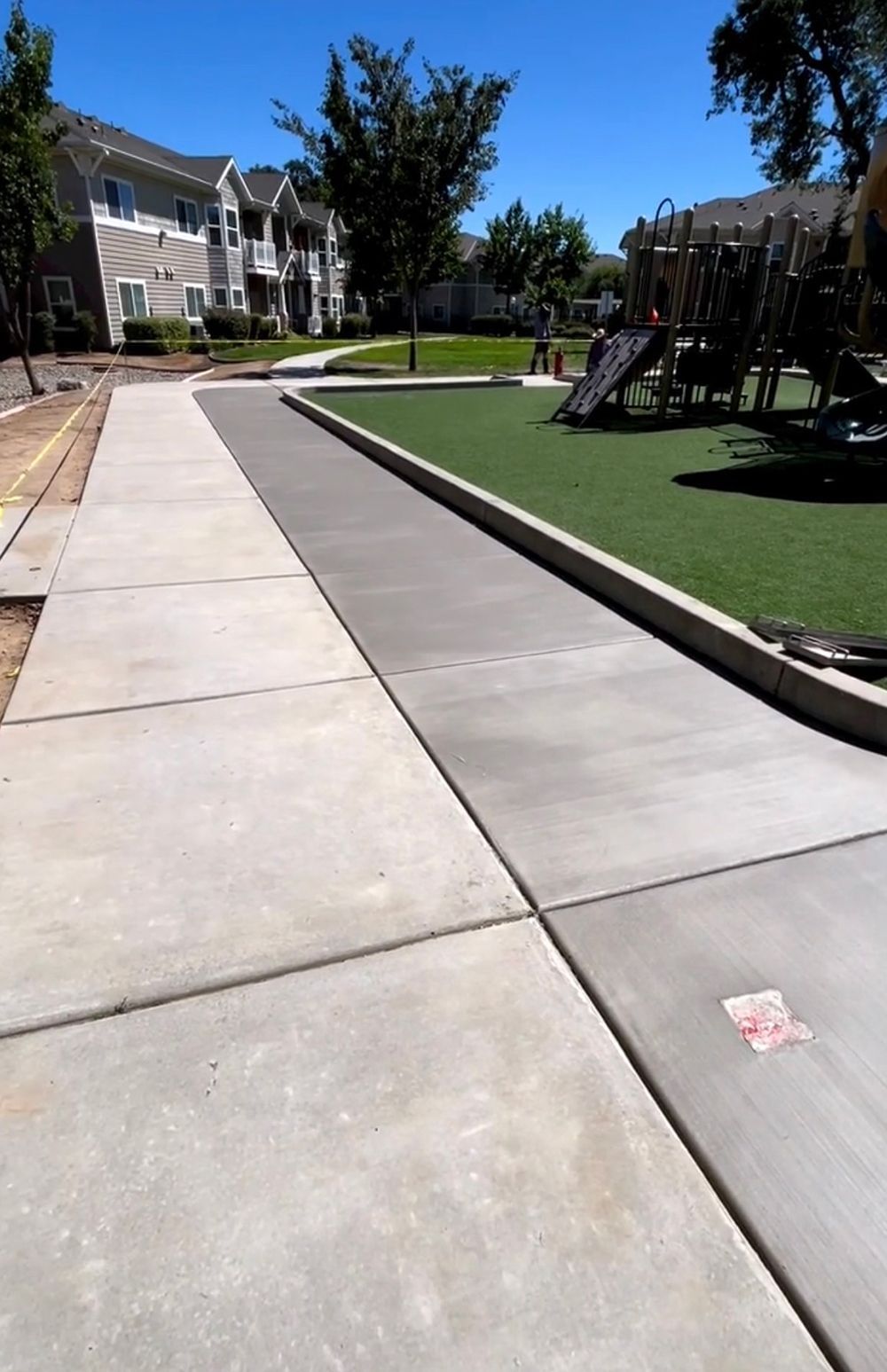 A concrete walkway leading to a playground with a house in the background