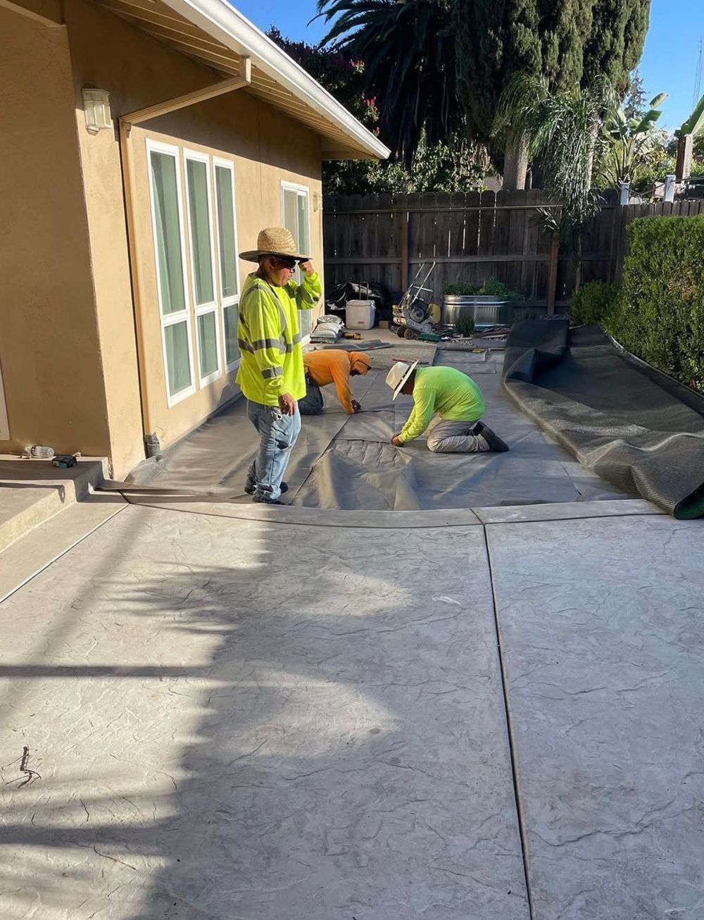 A group of construction workers are working on a concrete patio in front of a house.
