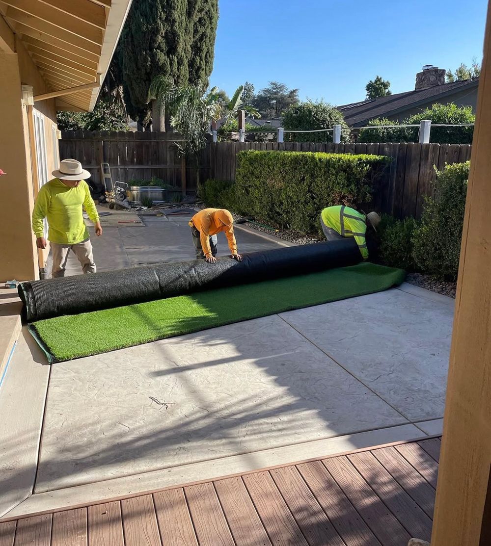 A man is laying a roll of artificial grass on a patio.