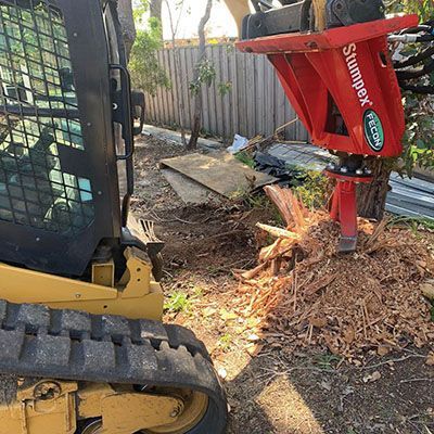 A bulldozer is cutting a tree stump in a yard.