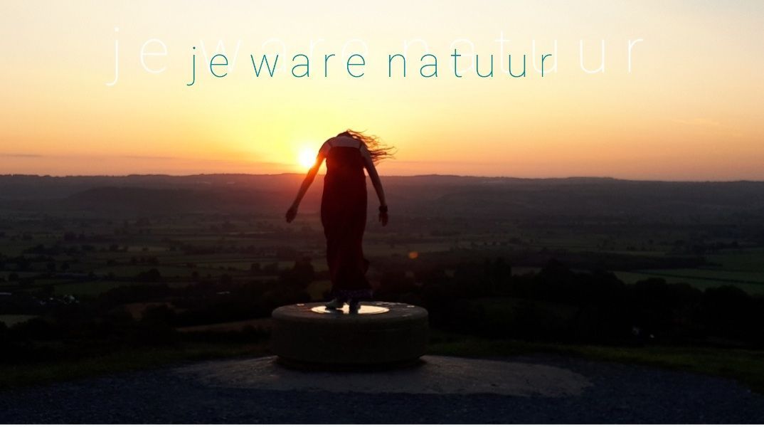 Iemand die in een notitieboekje op schoot schrijft; binnen, op een bank met kleurrijke kussens.