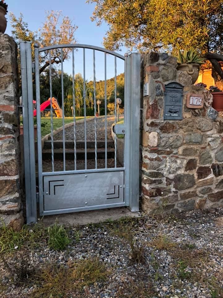 Cancello metallico incastonato nel muro di pietra, che conduce a un cortile con parco giochi.