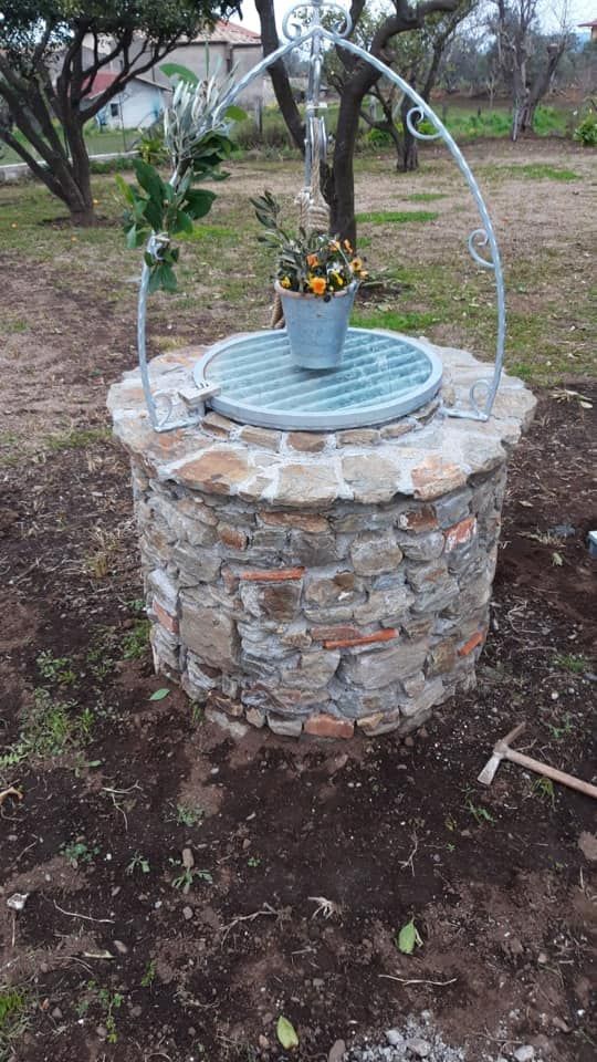 Pozzo in pietra con griglia metallica, decorato con fiori, in un ambiente esterno.