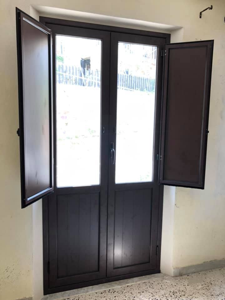 Doppie porte marroni con persiane, inserite in uno stipite bianco.