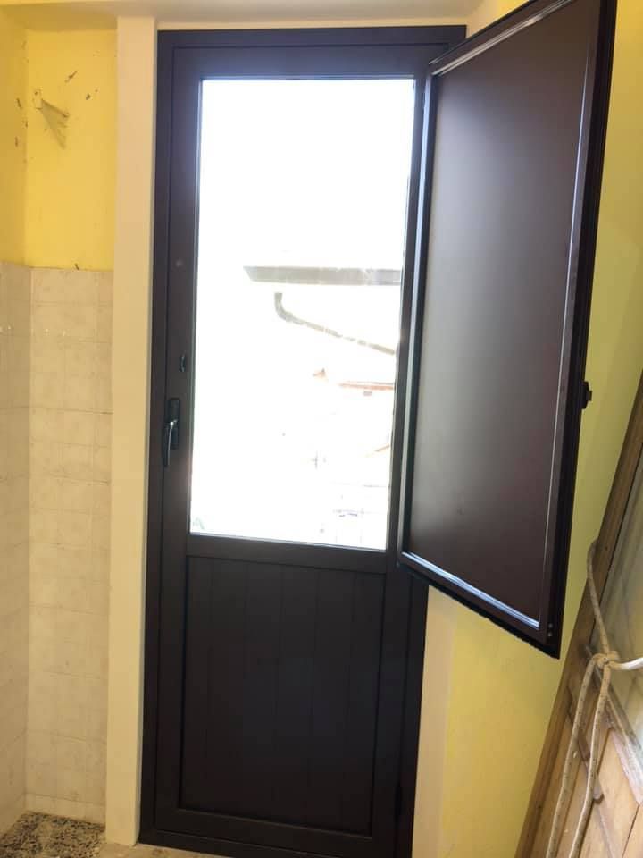 Porta marrone con un pannello aperto, contro una parete gialla, interno.