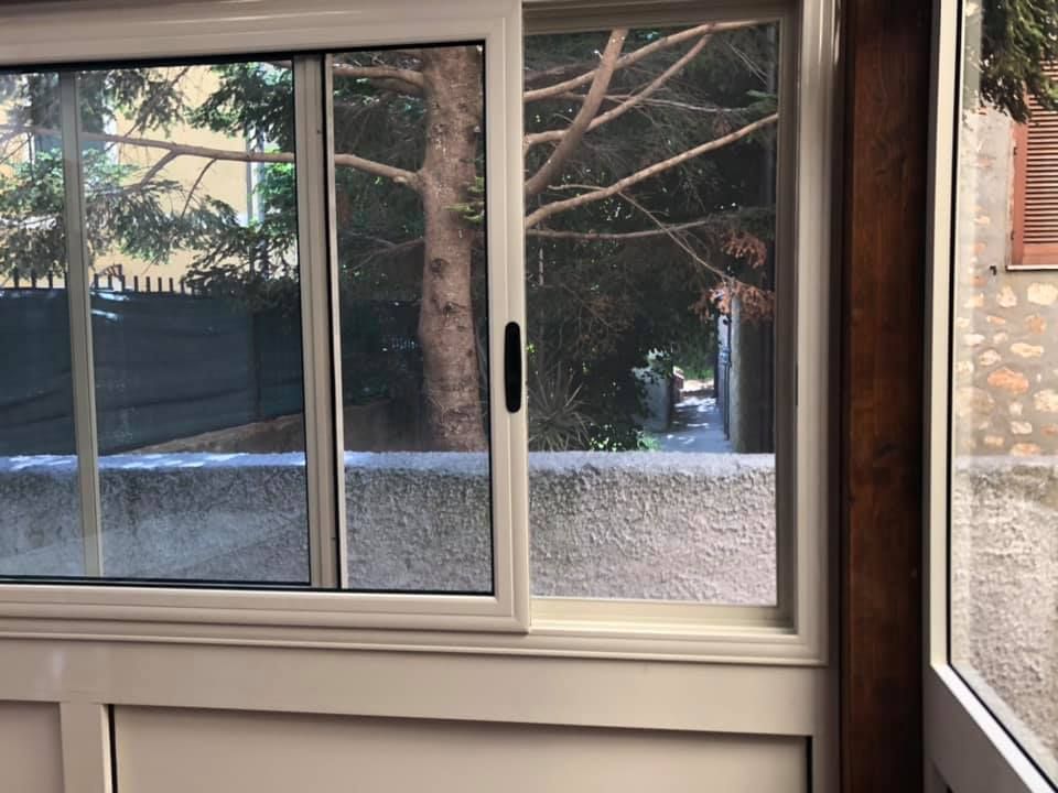 Finestra scorrevole con telaio bianco, aperta con vista sugli alberi e sull'esterno.