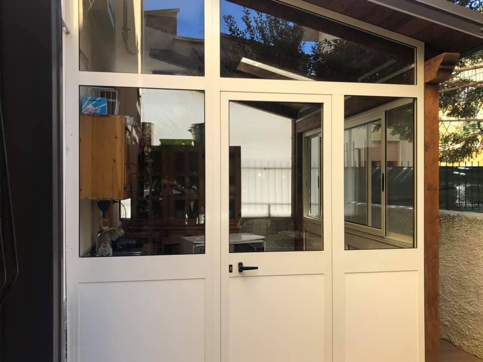 Porta in vetro con cornice bianca e finestre di una veranda con tetto in travi di legno, che riflettono l'esterno.