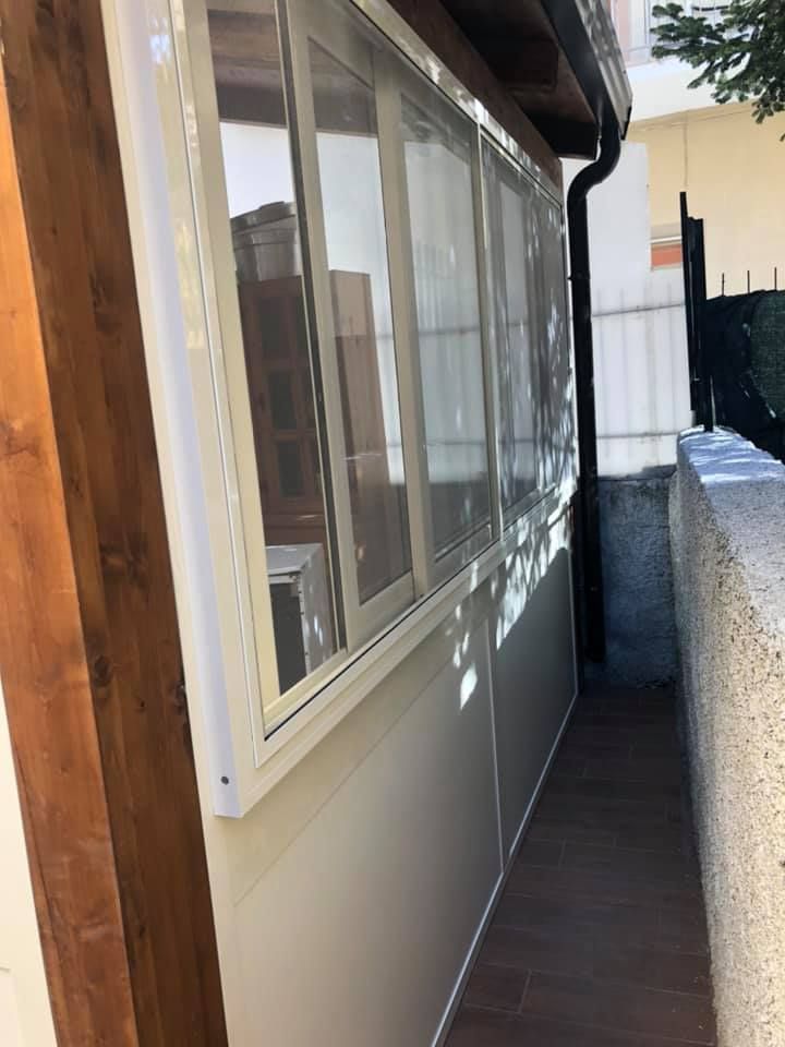 Veranda chiusa con pannelli in vinile trasparente, finiture bianche e trave in legno.