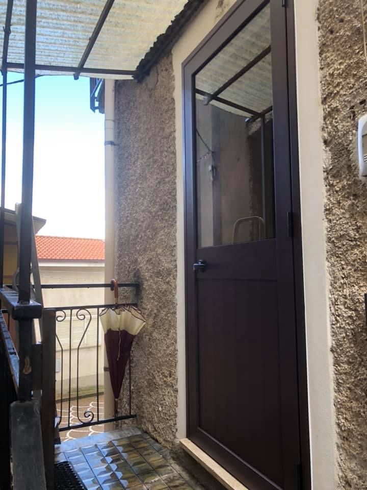 Porta marrone con pannello in vetro, su un balcone, accanto a una parete strutturata.