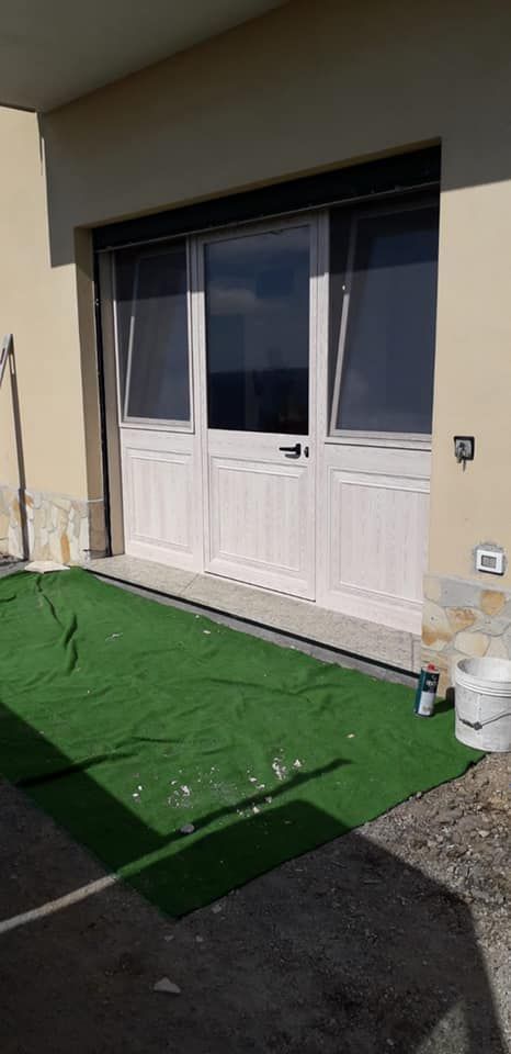 Porta dipinta di bianco con tappetino verde sul pavimento e secchio di vernice sul lato.