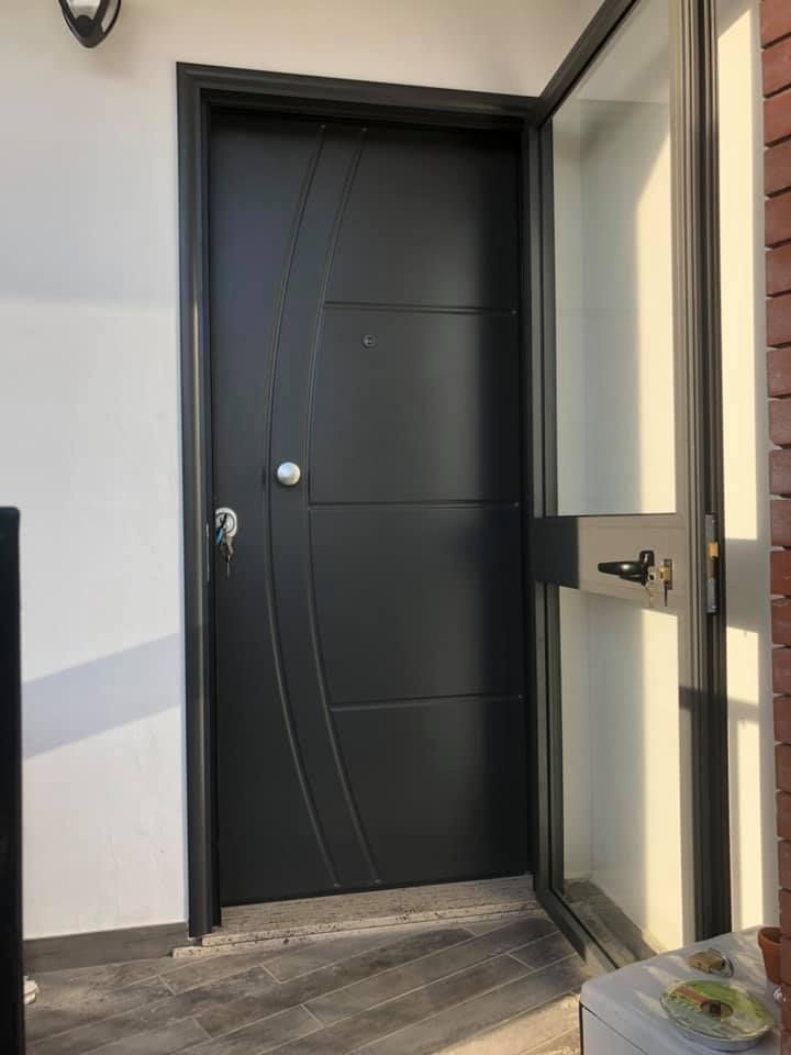 Porta d'ingresso nera con pannello laterale in vetro, chiavi nella serratura, inserita in un edificio con parete bianca.