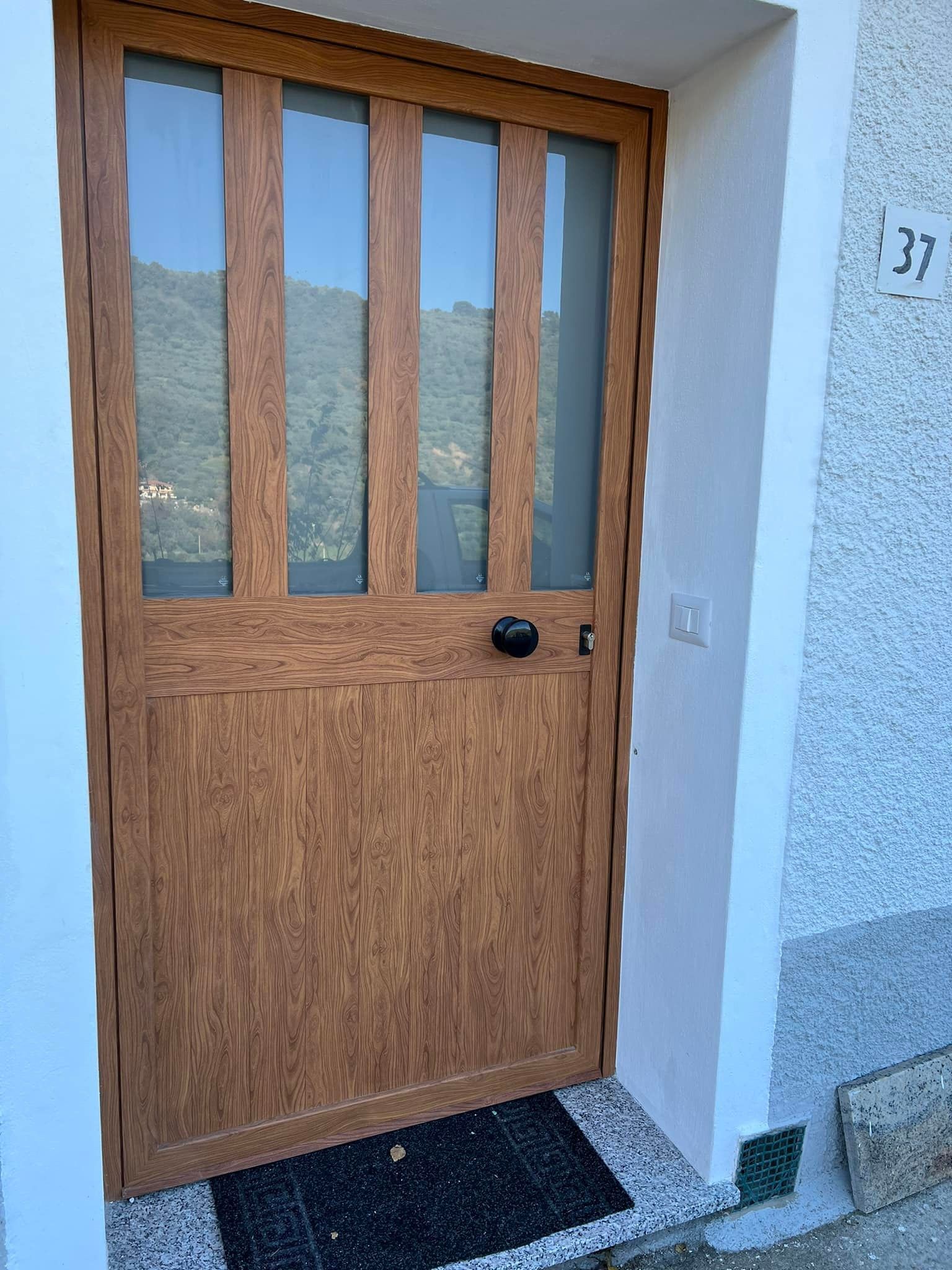 Porta in legno marrone con pannelli in vetro; maniglia nera; numero 37 sul muro.