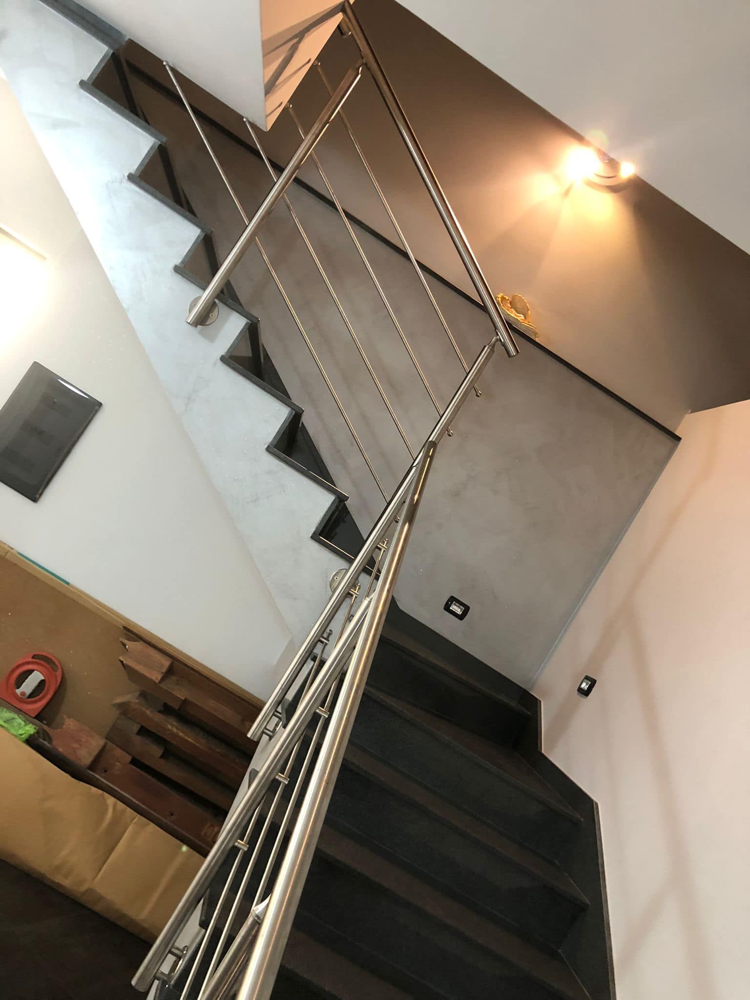 Scala con moderna ringhiera in acciaio inox; gradini in legno scuro, parete grigio chiaro.