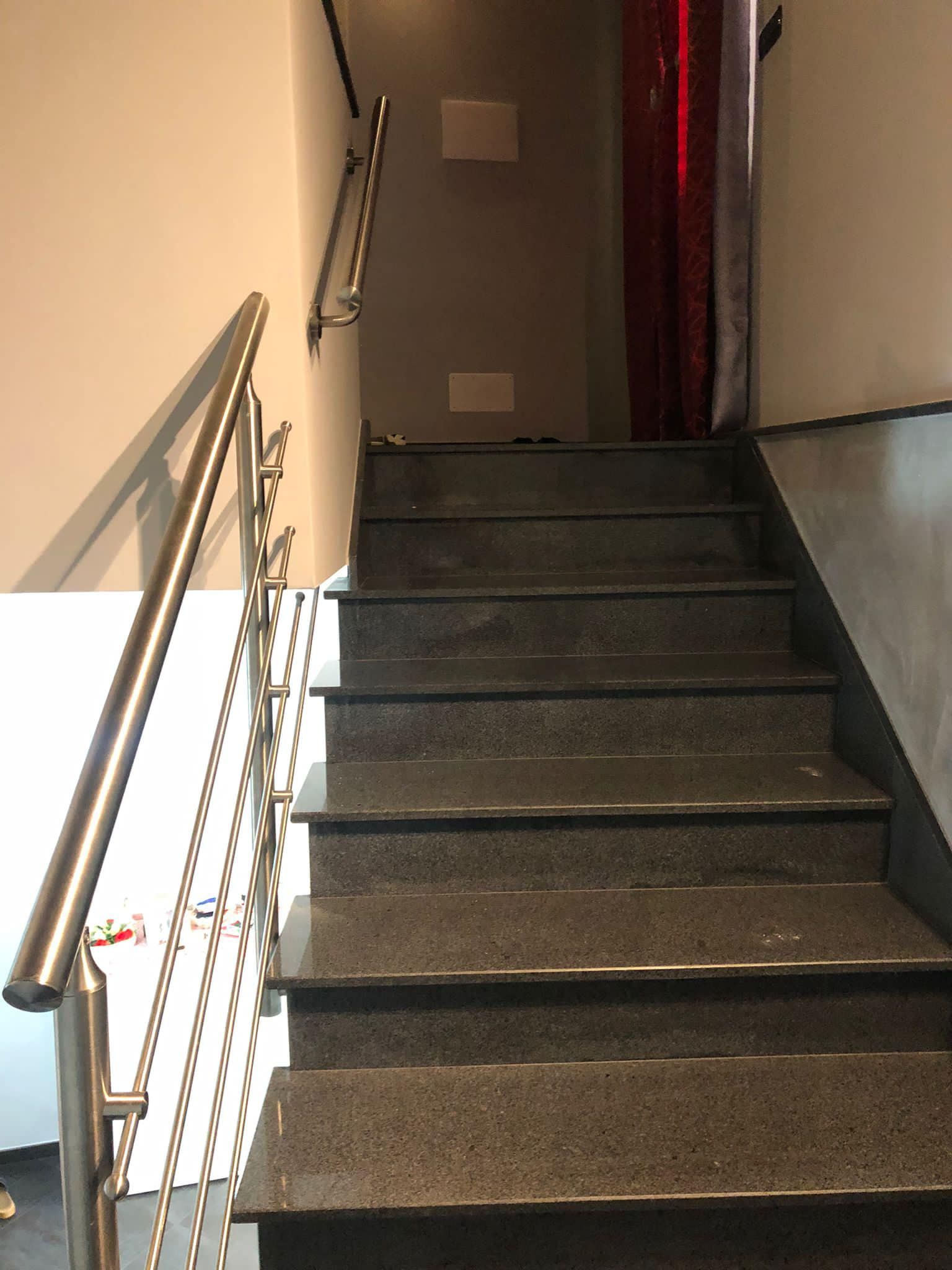 Scala con ringhiera in acciaio inossidabile e gradini in pietra scura, che sale verso un muro e tende rosse.