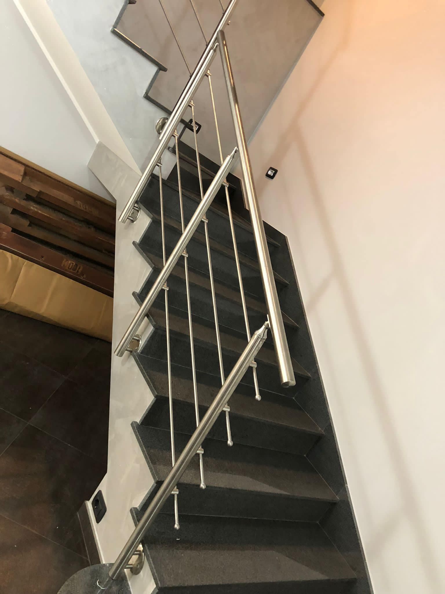 Scala con gradini scuri, ringhiera in acciaio inossidabile e pareti bianche.