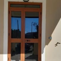 Porta doppia in legno con pannelli in vetro; inserita nella facciata di un edificio, colore marrone chiaro.