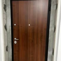 Una porta chiusa in legno marrone con cornice nera e ferramenta argentata in un portone in cemento.