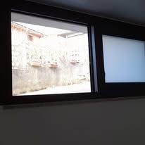 Due finestre con cornice scura, una trasparente e l'altra smerigliata, su una parete bianca. La finestra trasparente mostra una scena all'aperto.