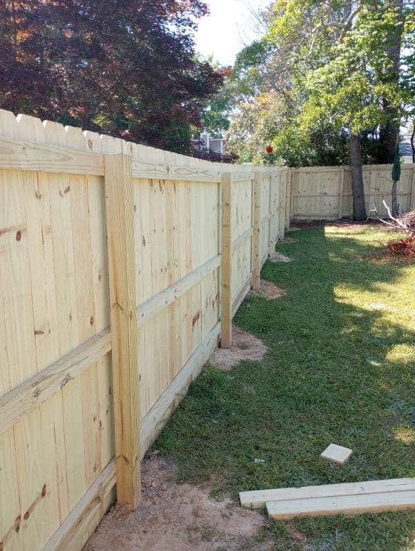 Wooden fence in a backyard with green grass and trees in the background.