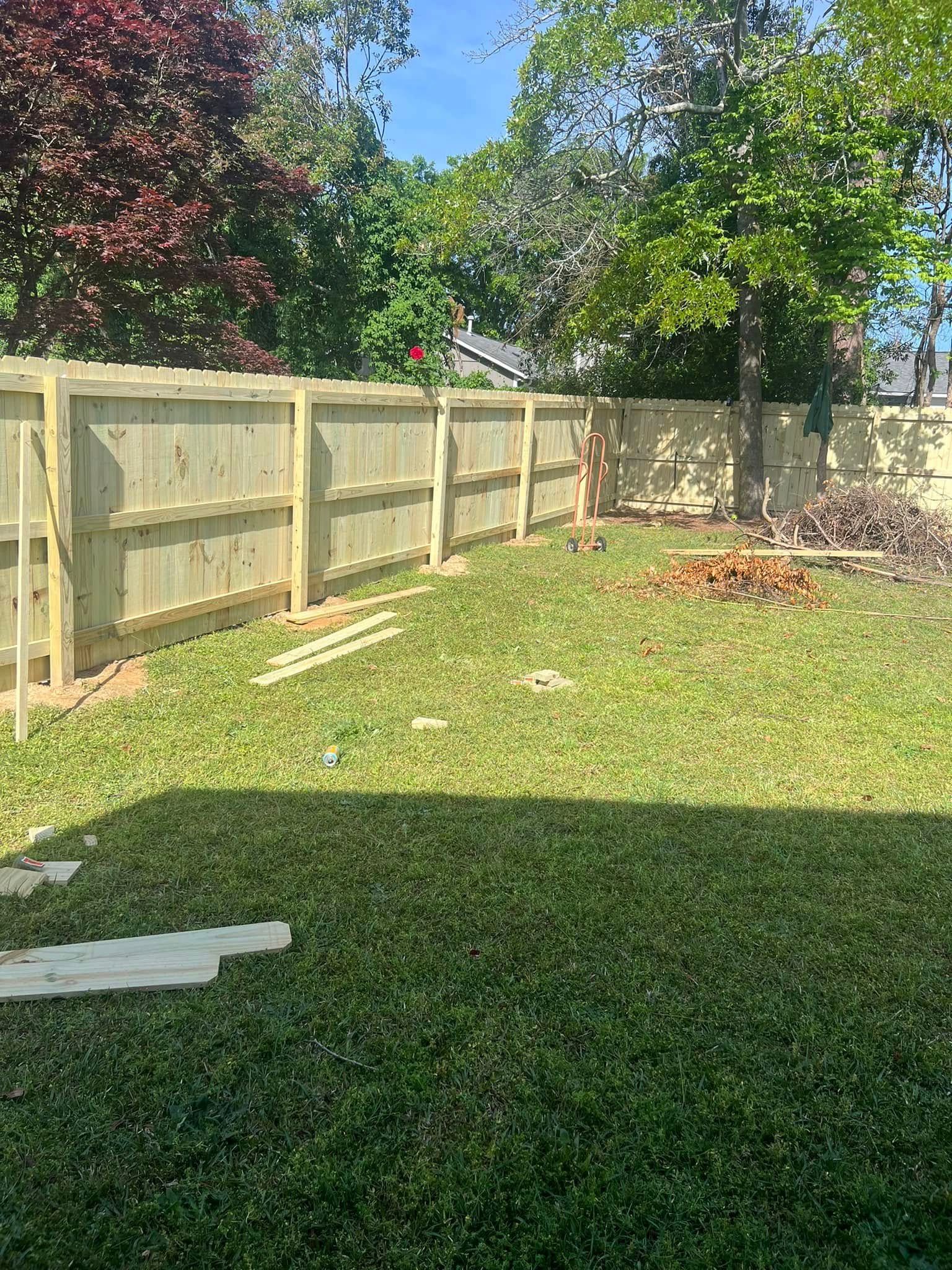 Wooden fence surrounds a grassy backyard with trees.
